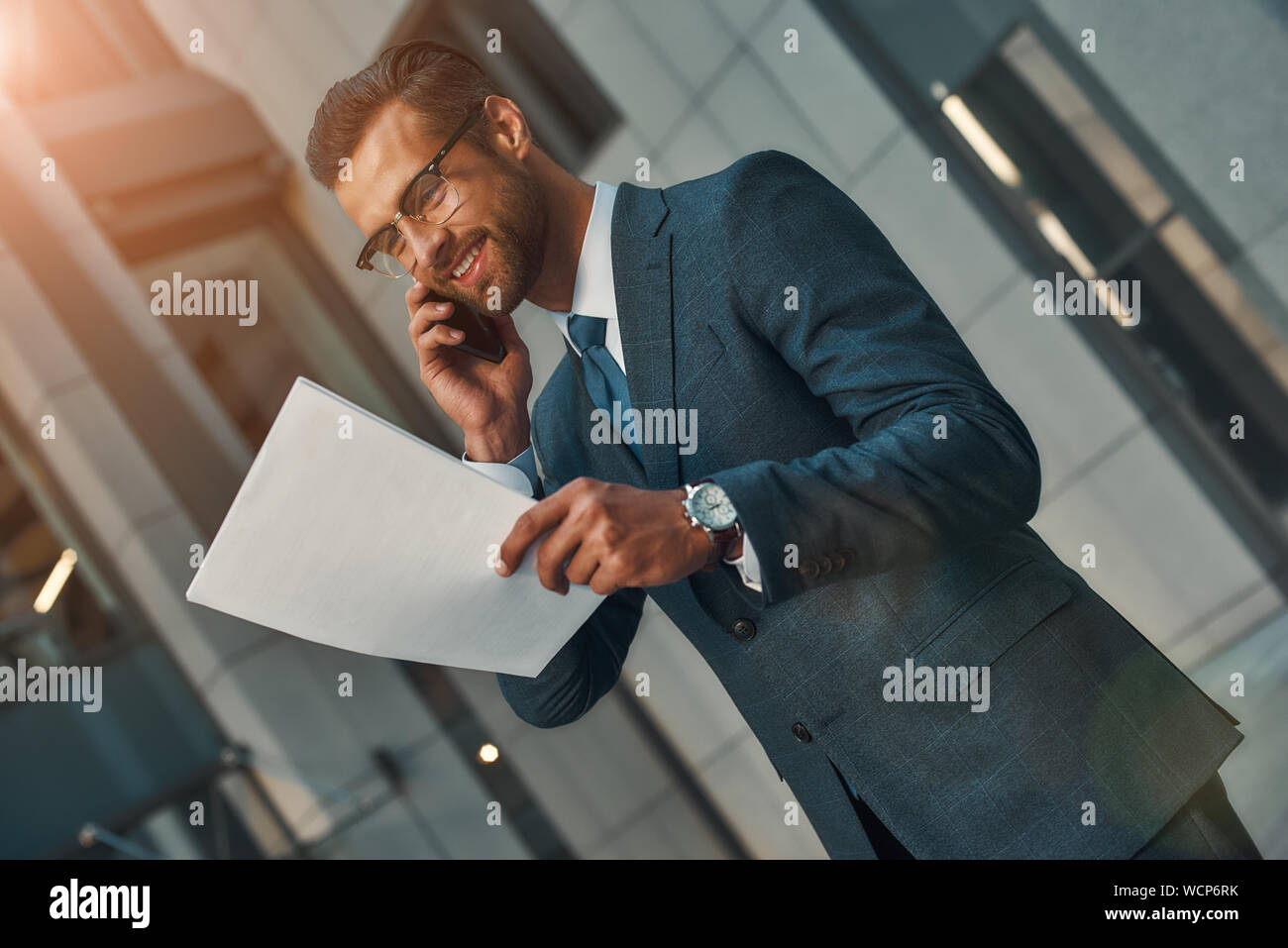 Ich habe tolle neue für Sie Portrait von lächelnden bärtigen Geschäftsmann in einen kompletten Anzug Gespräch per Telefon mit Kunden und den Blick auf Dokumente im Stehen im Freien. Business Konzept Stockfoto