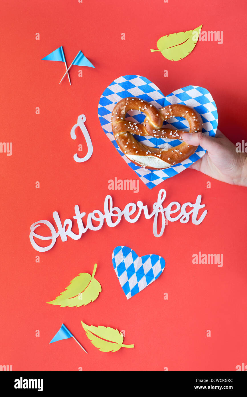 Papier Text "Ich Oktoberfest' Liebe. Flach auf Coral Farbe Papier Hintergrund mit Brezel in der Hand, dekorative Herzen, Flaggen und Blätter im Herbst. Stockfoto