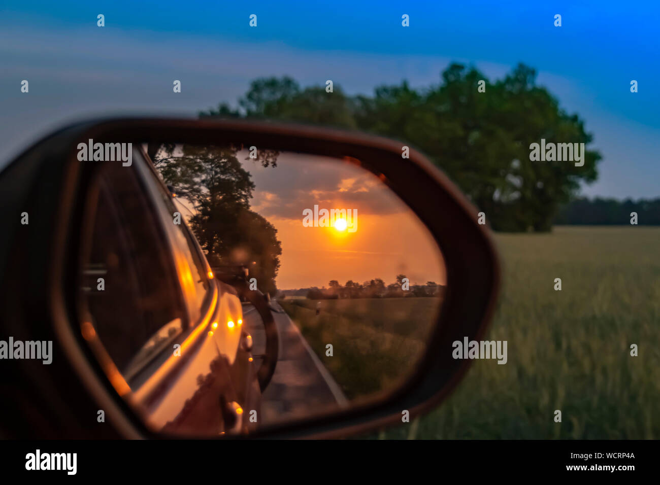 In den aussenspiegel von einem fahrenden Auto. In den Spiegel sehen Sie die  untergehende Sonne, Teile des Fahrzeugs und ein Fahrrad auf der Rückseite  Stockfotografie - Alamy