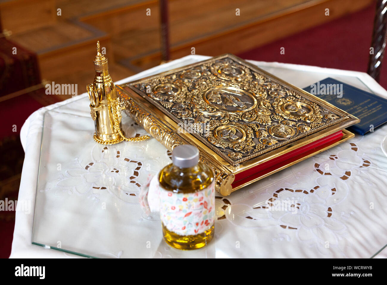 Elemente in einer Taufe, eine Flasche Öl und eine evangel, während der Vorbereitung einer traditionellen griechischen Orthodoxen Taufe. Stockfoto