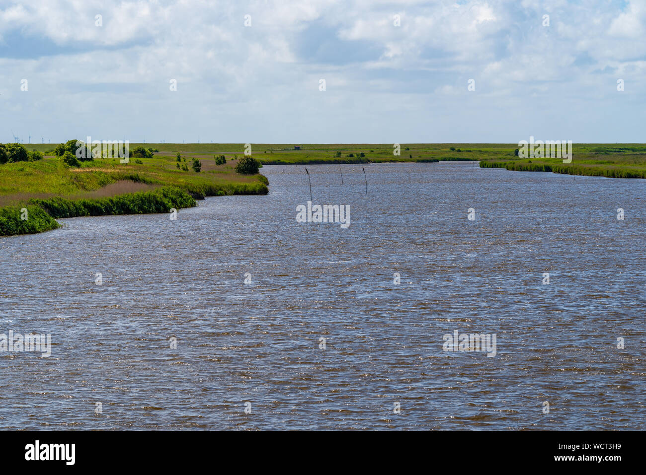 Blick über einen Kanal mit dramatischen Wolken im blauen Himmel in Friesland, Niedersachsen, Deutschland Stockfoto