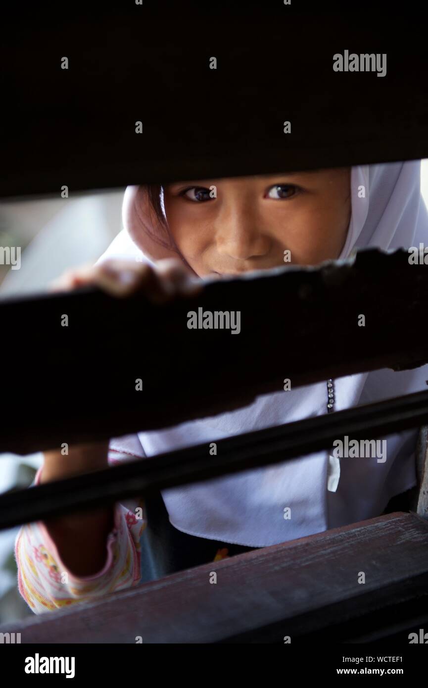 Kinder schauen durch einen Schlitz in der Klasse Fenster an der Madrasa Aziza Al-Islamia in Barangay Polonuling in Tupi Gemeinde in der Provinz South Cotabato. Balik Tahderiyyah Tahderiyyah ist ein Weg der Partnerschaft innerhalb der Gemeinschaft zu fördern. Er betont den Wert der Freiwilligenarbeit, die Zusammenführung der Lehrer, mudeers (Administratoren), Eltern und andere Akteure innerhalb einer Gemeinschaft zusammen zu arbeiten. Die Tahderiyyah Programm ist eine integrierte Frühkindliche Bildung Programm für junge Kinder in schwer zu erreichenden Bereichen aufgrund der Entfernung und der Präsenz von bewaffneten Konflikten, die in den REACH Stockfoto