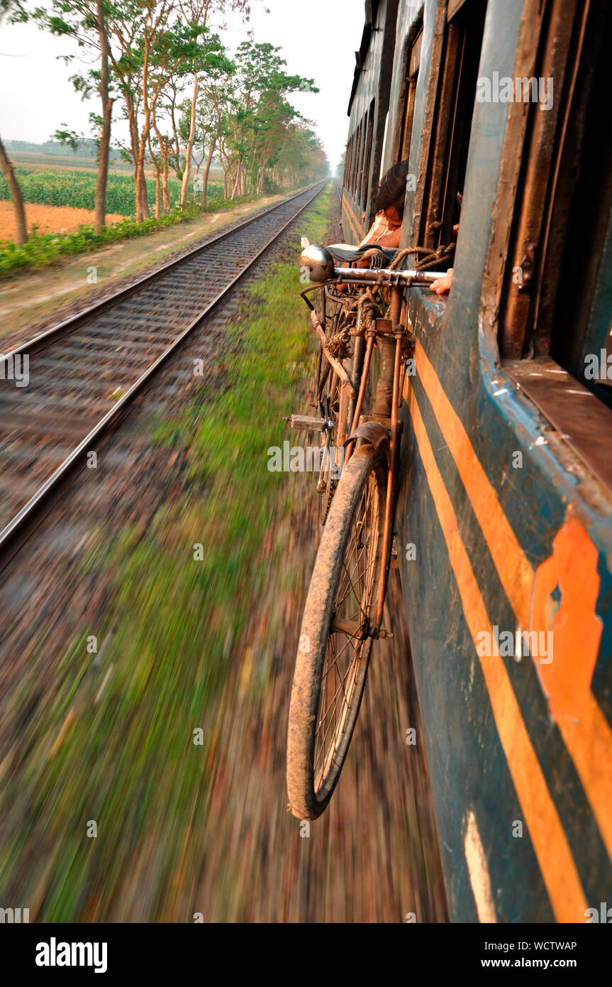 Ein Fahrrad hängt an einem Fenster von einem Zug durch die Landschaft bewegen, in Bangladesch. März 21, 2011. Stockfoto
