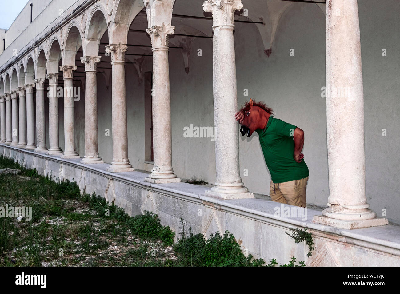 Mann mit einem Pferd Kopf Maske ist gegen eine Spalte unter einem alten Kloster und denkt über sein Leben. Probleme, Persönlichkeit, Mystik, aber Stockfoto