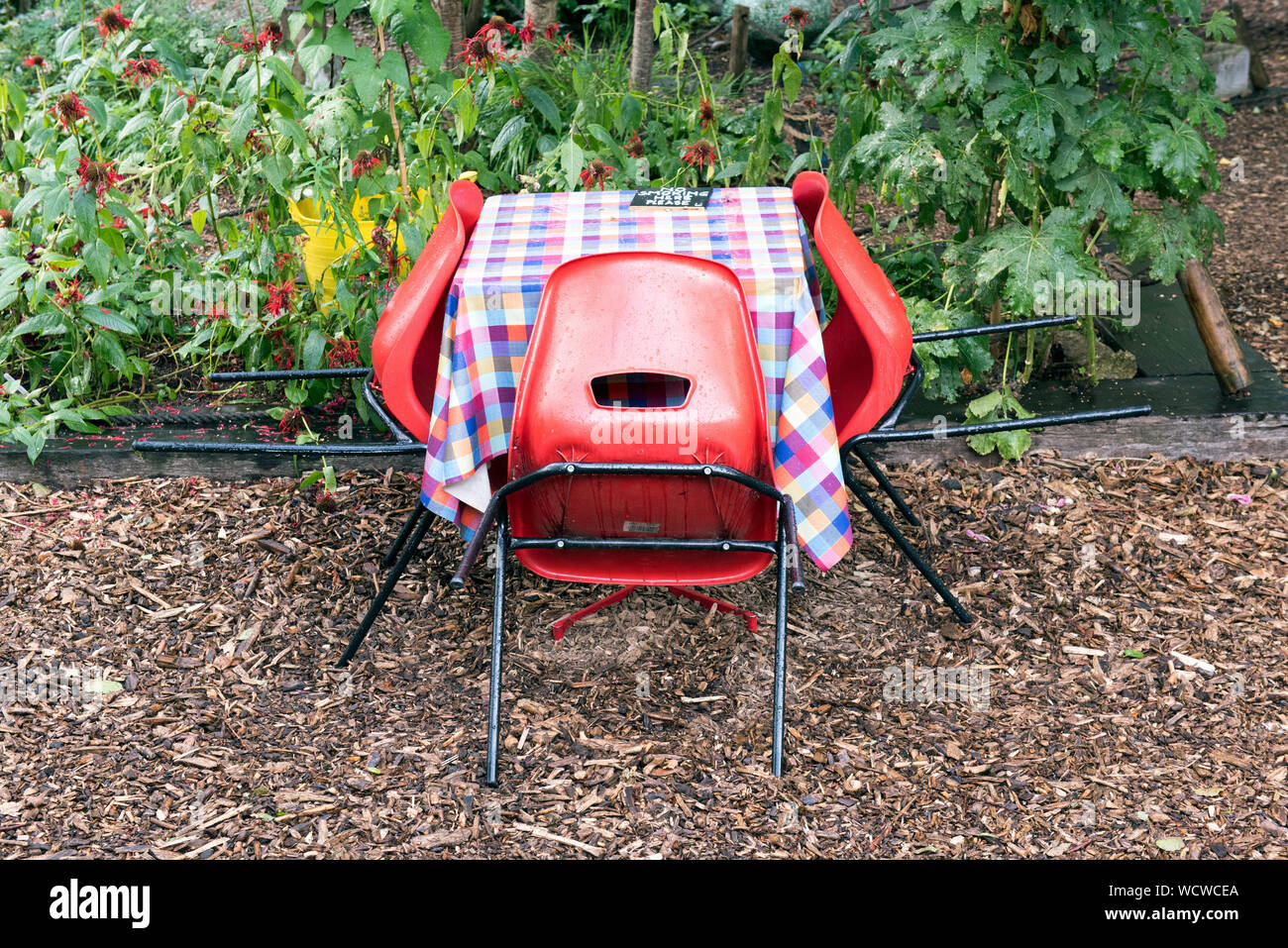 Leere Tabelle mit chequred Tischdecke und drei rote Stühle draußen im Regen, Dalston östlichen Kurve Garten, Kanzleien. Stockfoto