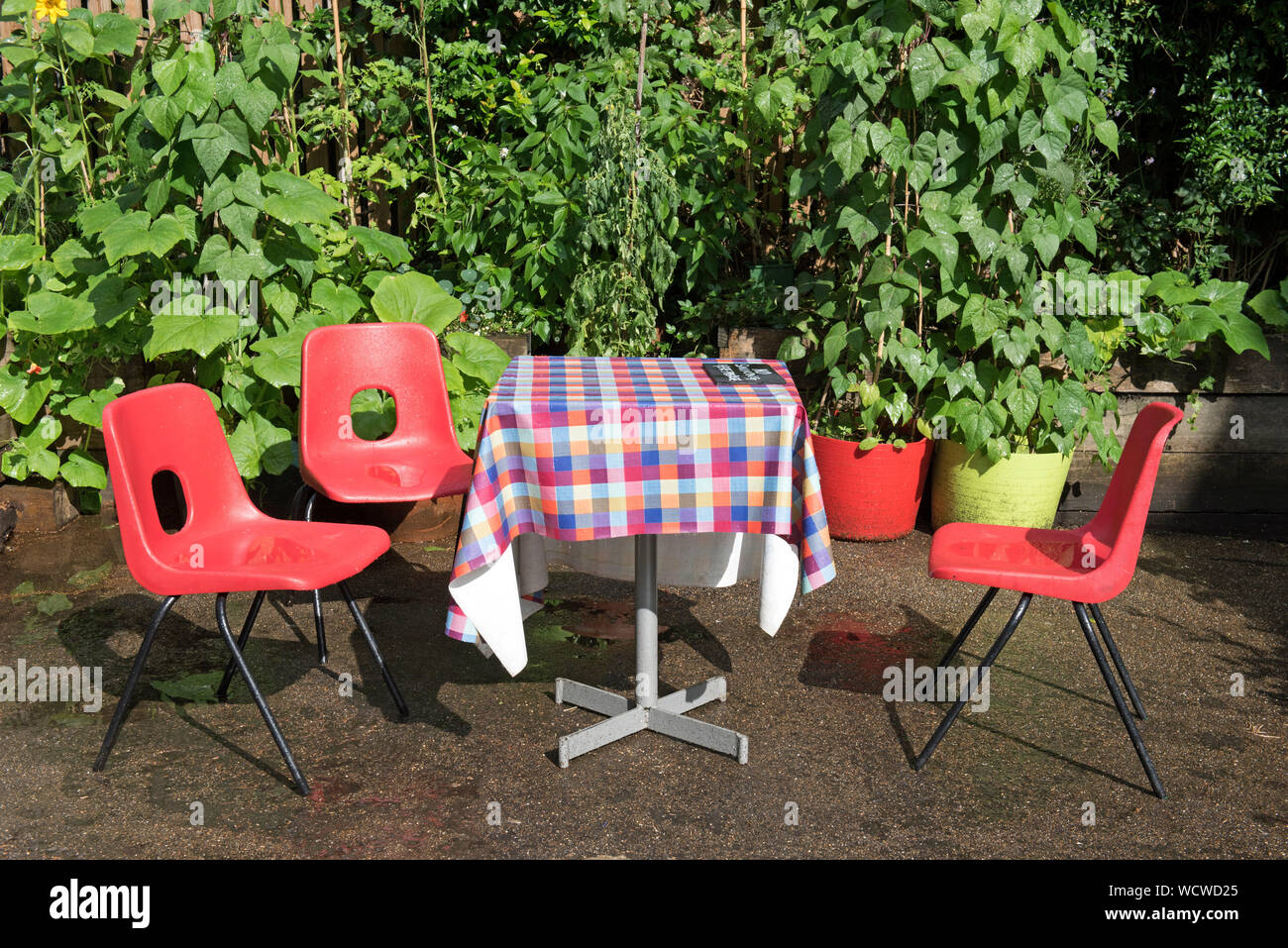 Leere Tabelle mit chequred Tischdecke und drei rote Stühle draußen im Regen, die sich auf Sitze Dalston östlichen Kurve Garde, Kanzleien, Stockfoto