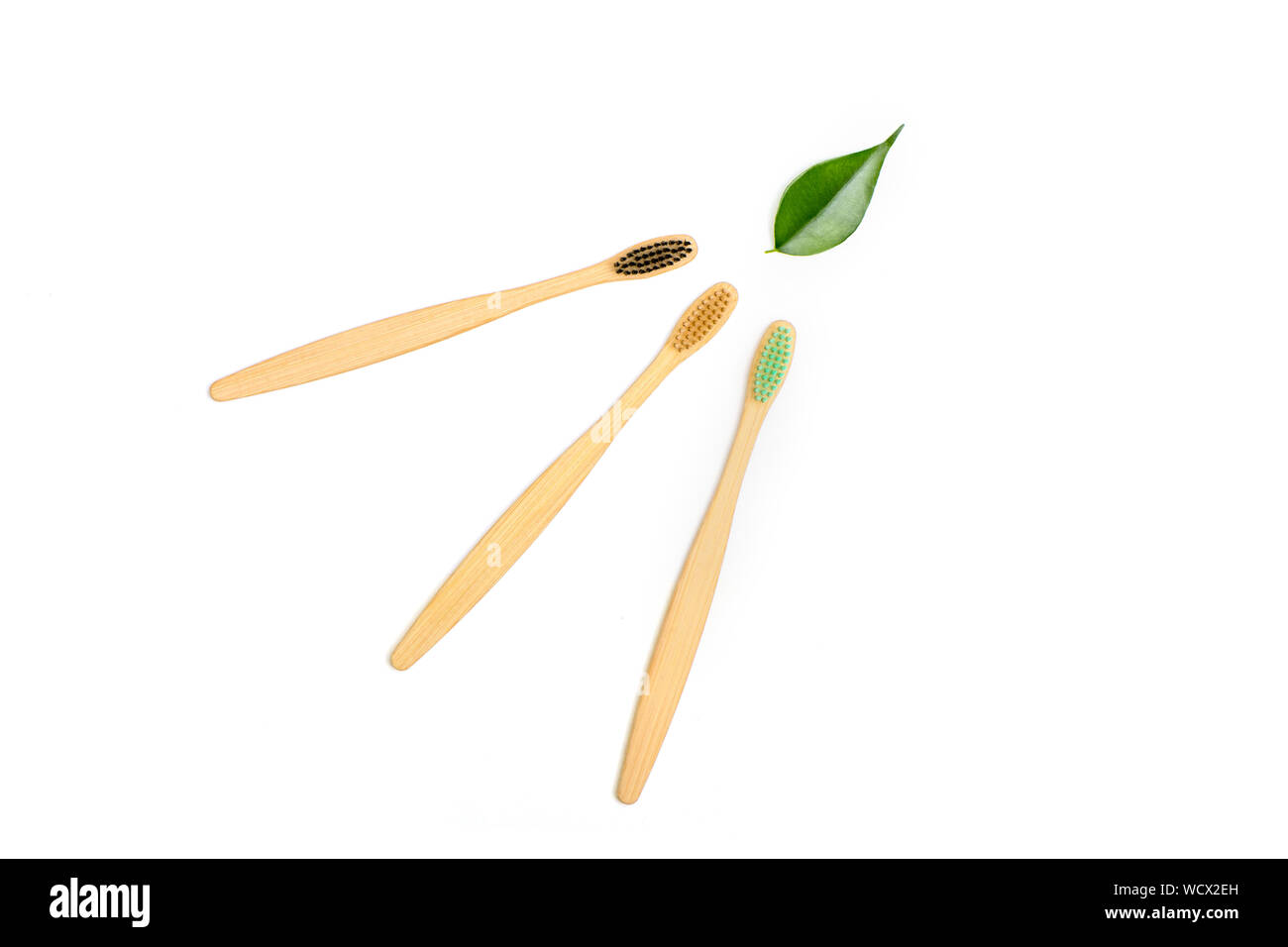 Satz von drei natürlichen Holz Bambus Zahnbürsten mit grünen Blättern auf weißem Hintergrund. Kunststoff Konzept. Stockfoto