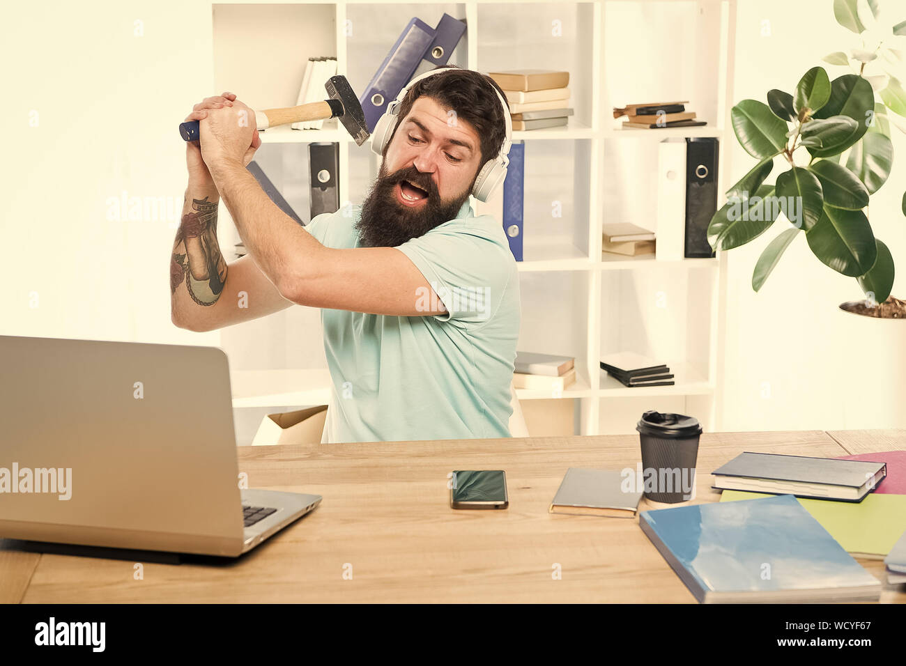 Langsame Internetverbindung. Veraltete Software. Computer lag. Gründe für Computer zurückbleiben. Wie fix langsam hinterher. Hasse office Routine. Man bärtige Kerl Kopfhörer Büro schwingen Hammer auf dem Computer. Stockfoto