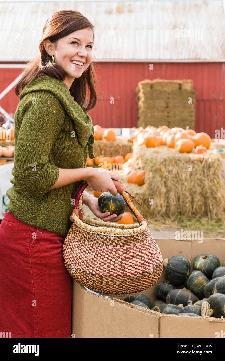 Glücklich lächelnde junge Frau Einkaufen für frisches Gemüse squash im Freien an einem Bauernhof stehen. Sie ist legere Herbst Mode cord Rock ein Stockfoto