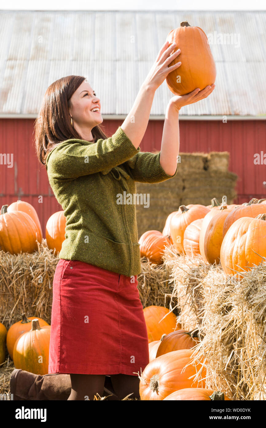 Glücklich lächelnde junge Frau Einkaufen für Kürbisse im Freien an einem Bauernhof stehen. Sie ist legere Herbst Mode cord Rock und Pullover. Stockfoto