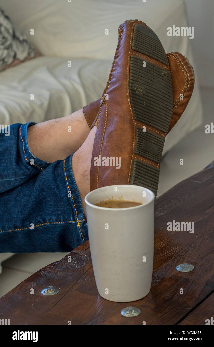 Füße mit Leder Schuhe auf einem Tisch isoliert Neben einer Tasse Kaffee Bild im Hochformat Stockfoto