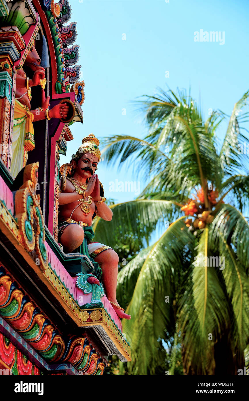 Steinstatue der Hindu indische Gottheit im Gebet an der Seite der bunten Tempel Wand in Singapur mit Palme in Soft Focus Hintergrund in Hochformat Stockfoto
