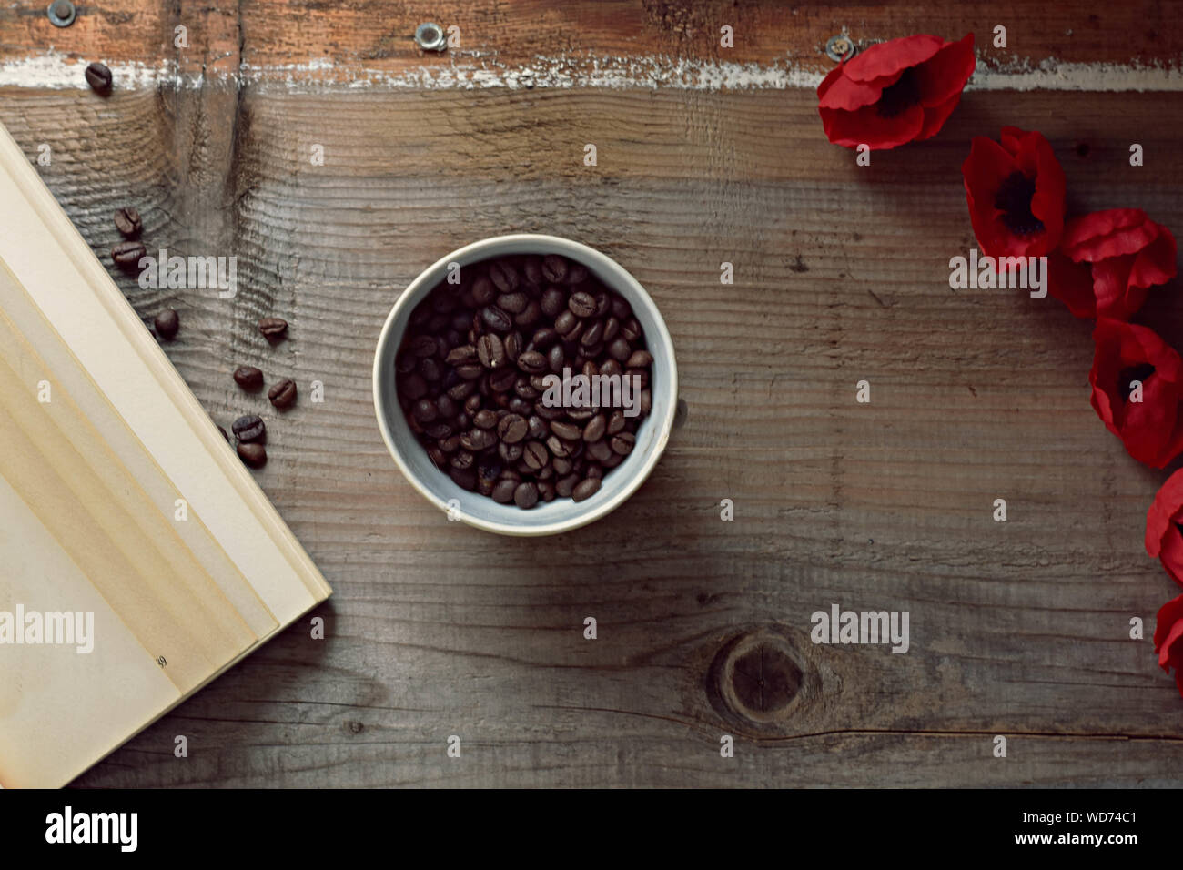 Kaffeebohnen, alte Buch und rote Blumen auf Holz- Hintergrund Stockfoto