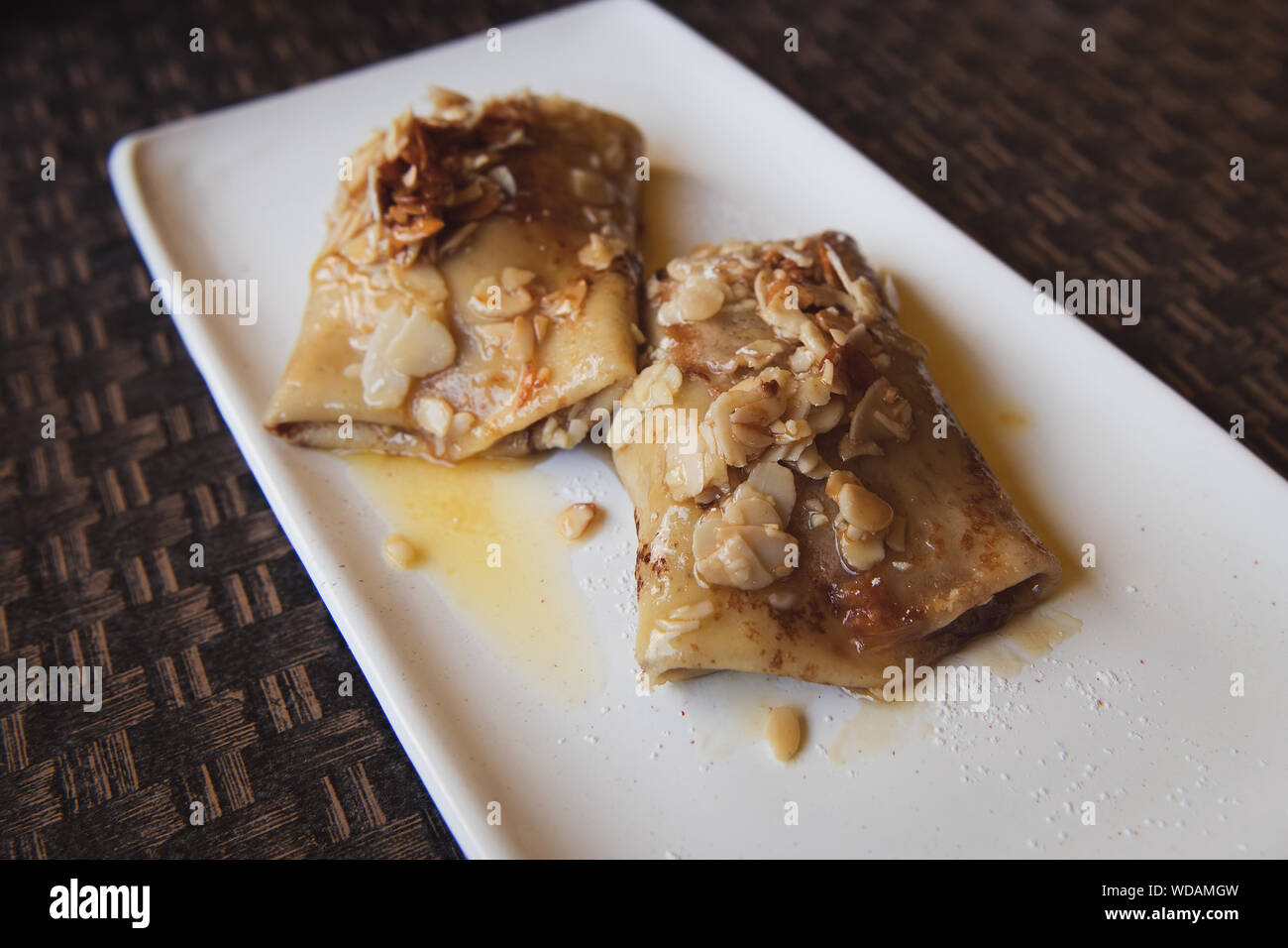 Russische Pfannkuchen mit Quark füllen und gehobelten Mandeln und Honig auf der Oberseite. Köstliches Dessert auf dem weißen Teller. Stockfoto