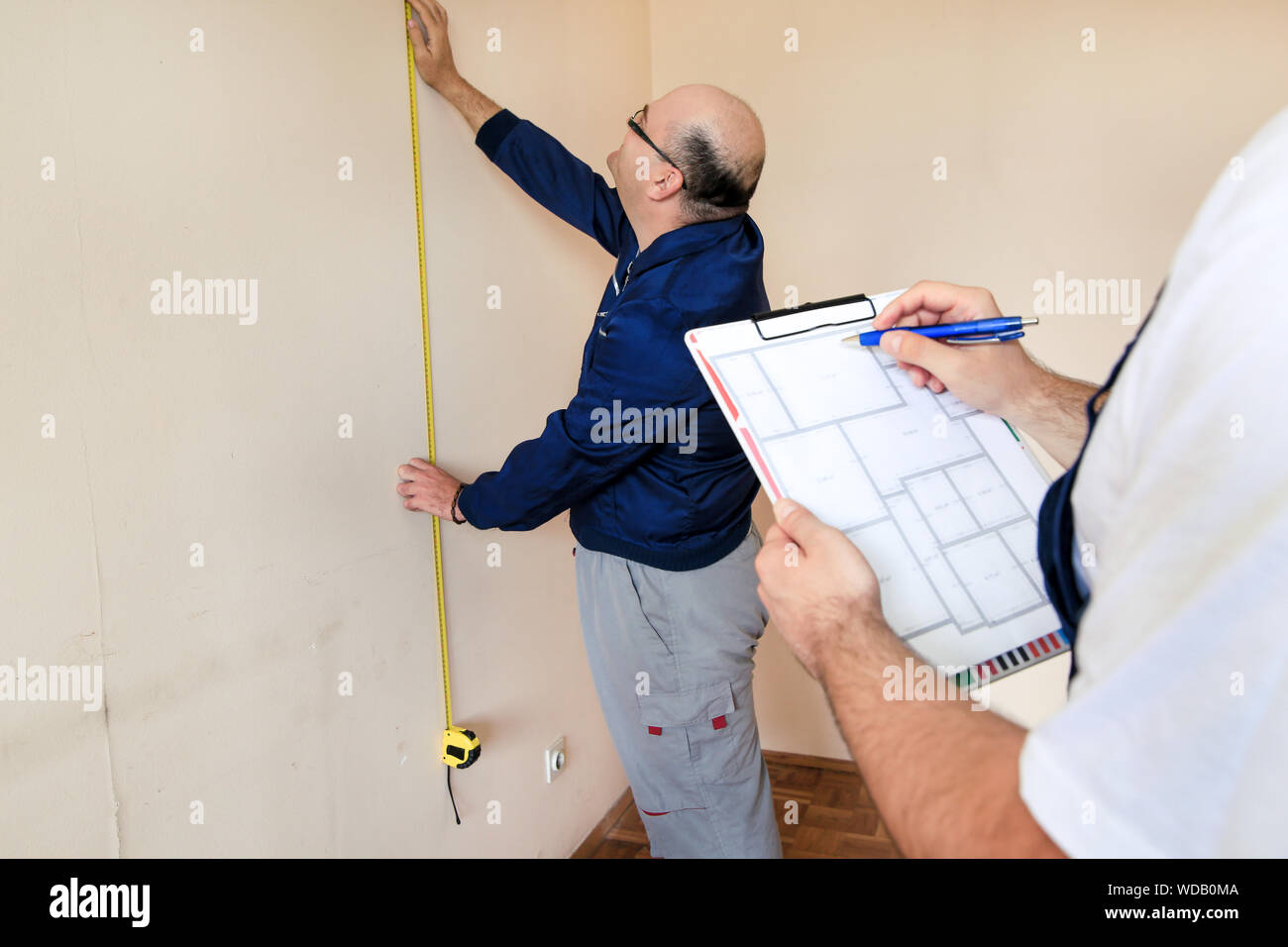 Ingenieur, Auftragnehmer und Projektleiter mit seinem Kollegen, Bauarbeiter, Handwerker und Baumeister ist die Messung an der Wand des Zimmers mit Maßband. Stockfoto