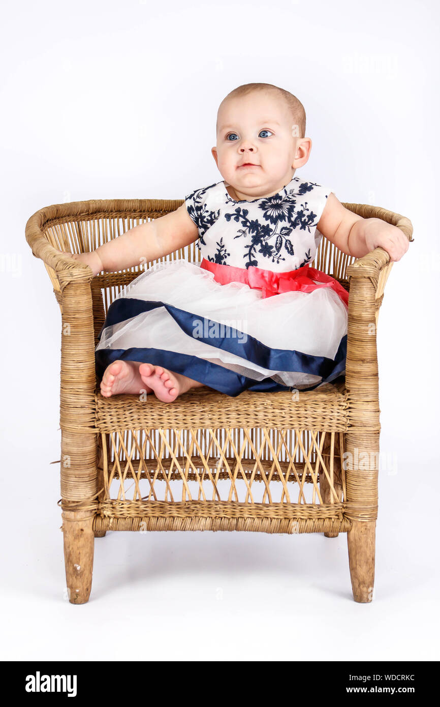 6 Monate alten Baby Mädchen in ein niedliches Kleid sitzt auf einem rattan Stuhl Stockfoto