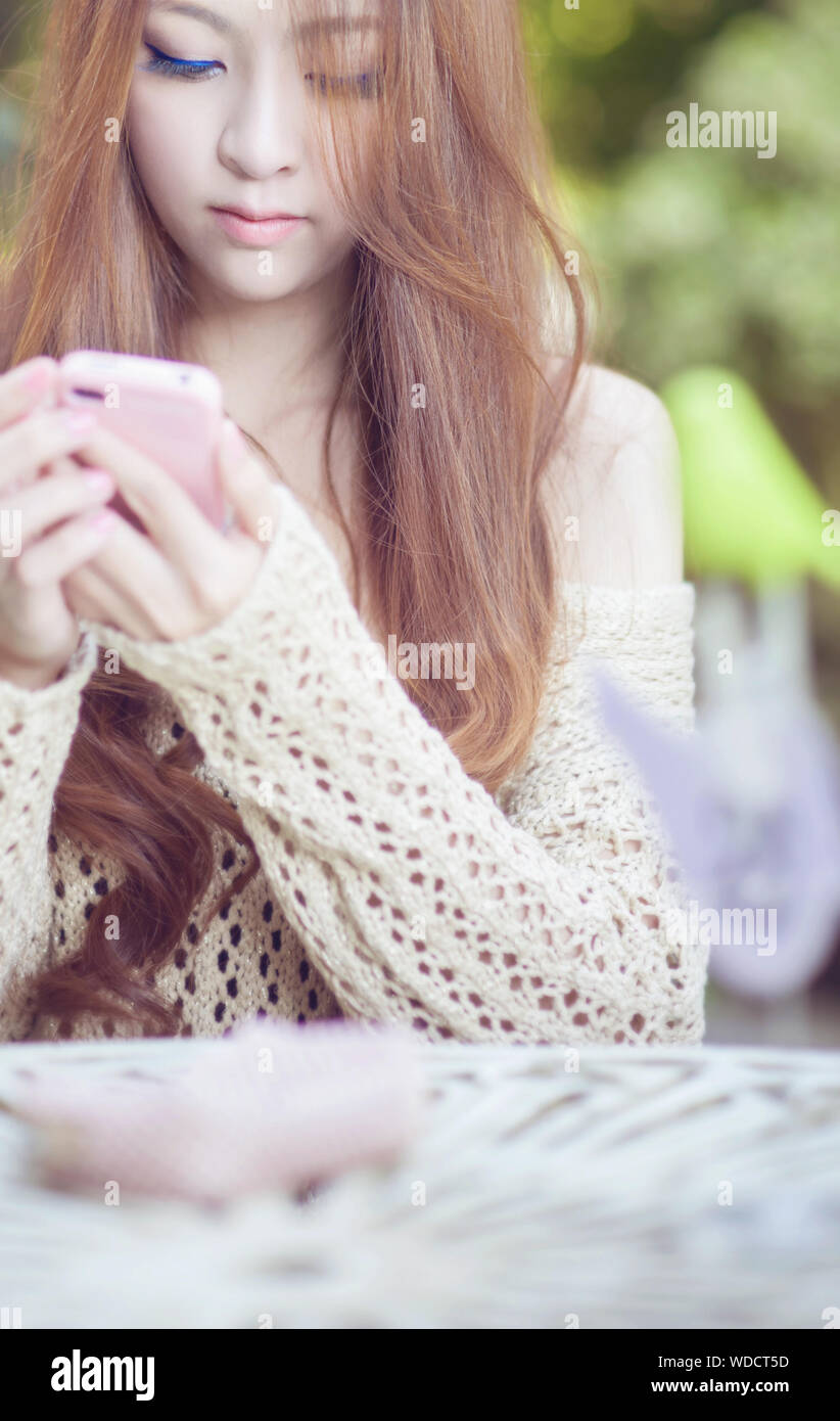 Junge Frau mit Telefon, beim Sitzen am Tisch Stockfoto