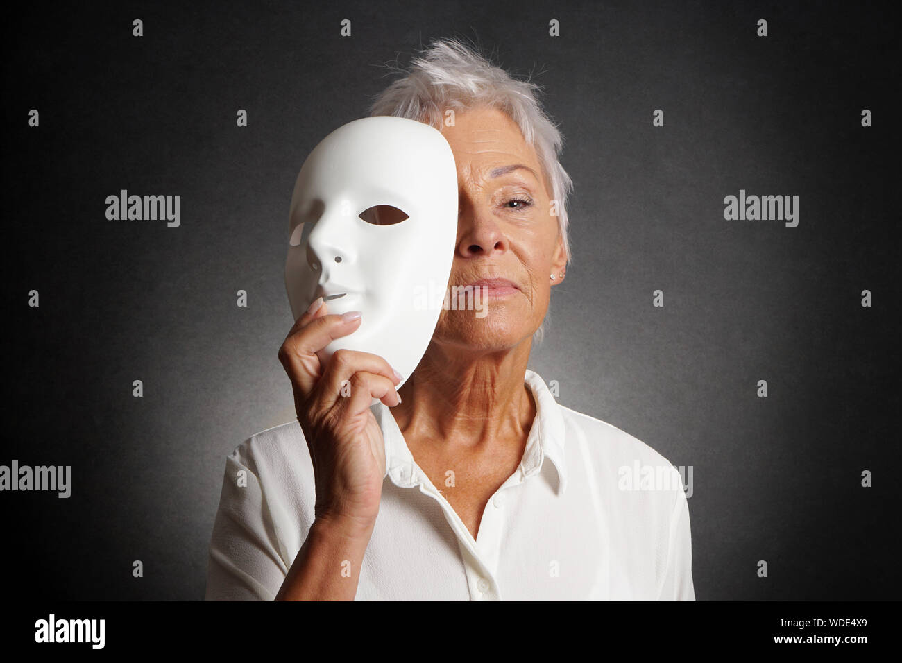 Ernsthafte ältere Frau offenbart wahres Gesicht hinter der Maske suchen Stockfoto