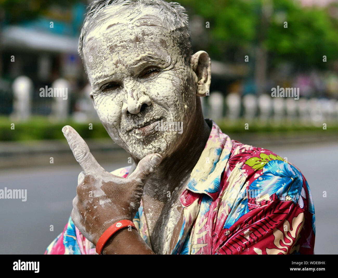 Lustig Thai Mann hat sein Gesicht und bunten Hemd mit einem weisse Paste während Songkran abgedeckt und verhöhnt den Fotografen mit einer V-Zeichen von Art. Stockfoto