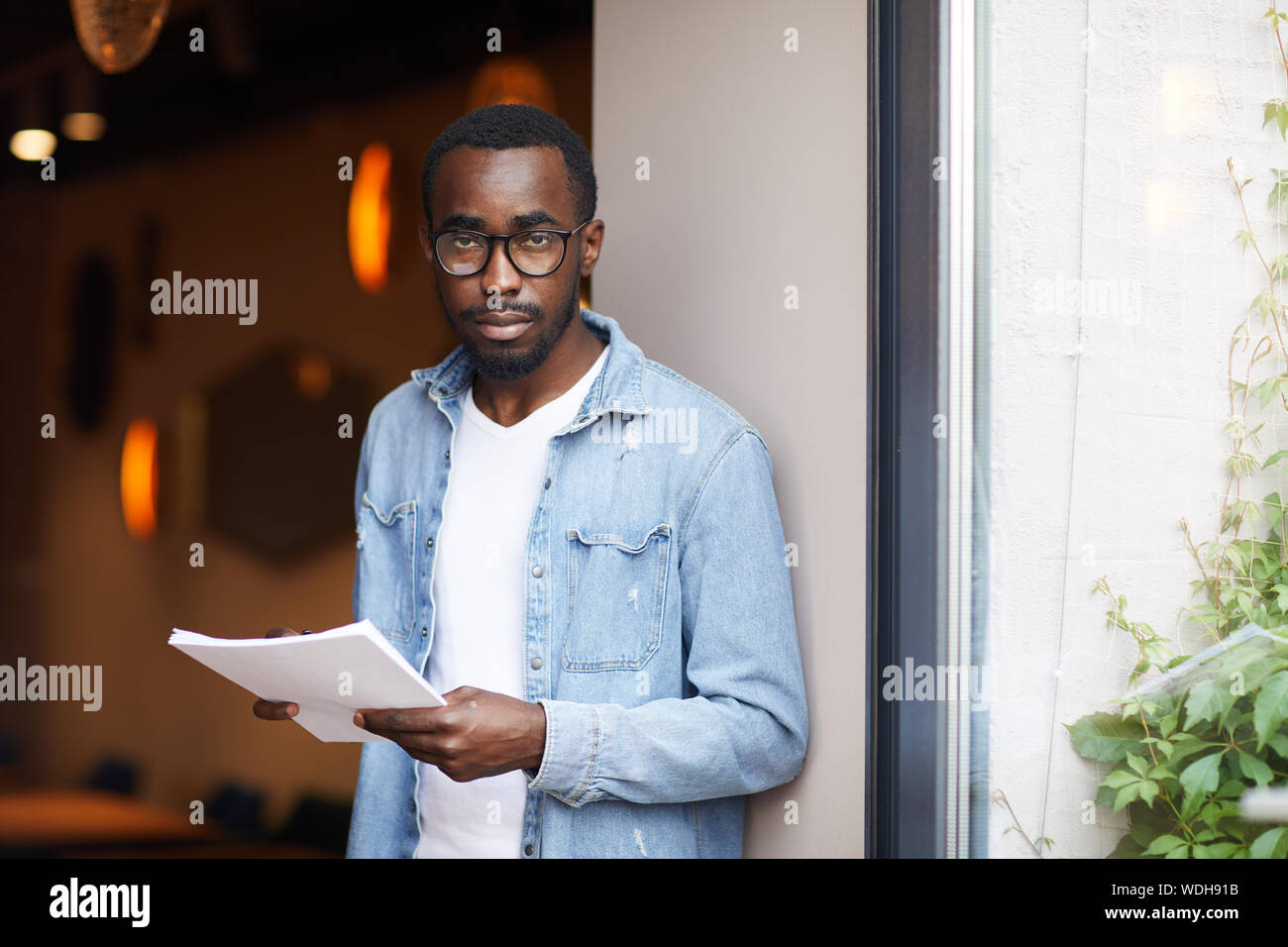 Portrait der Afrikanischen jungen Mann in Brillen und legere Kleidung, Dokumente und Kamera Stockfoto