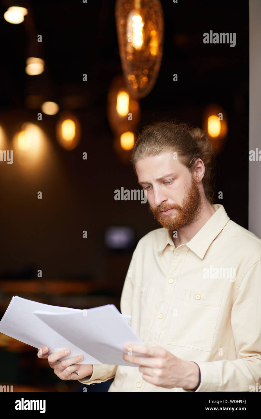 Ernsthafte junge rothaarige Mann hält Dokumente in seine Hände und Prüfung beim stehen im Restaurant Stockfoto
