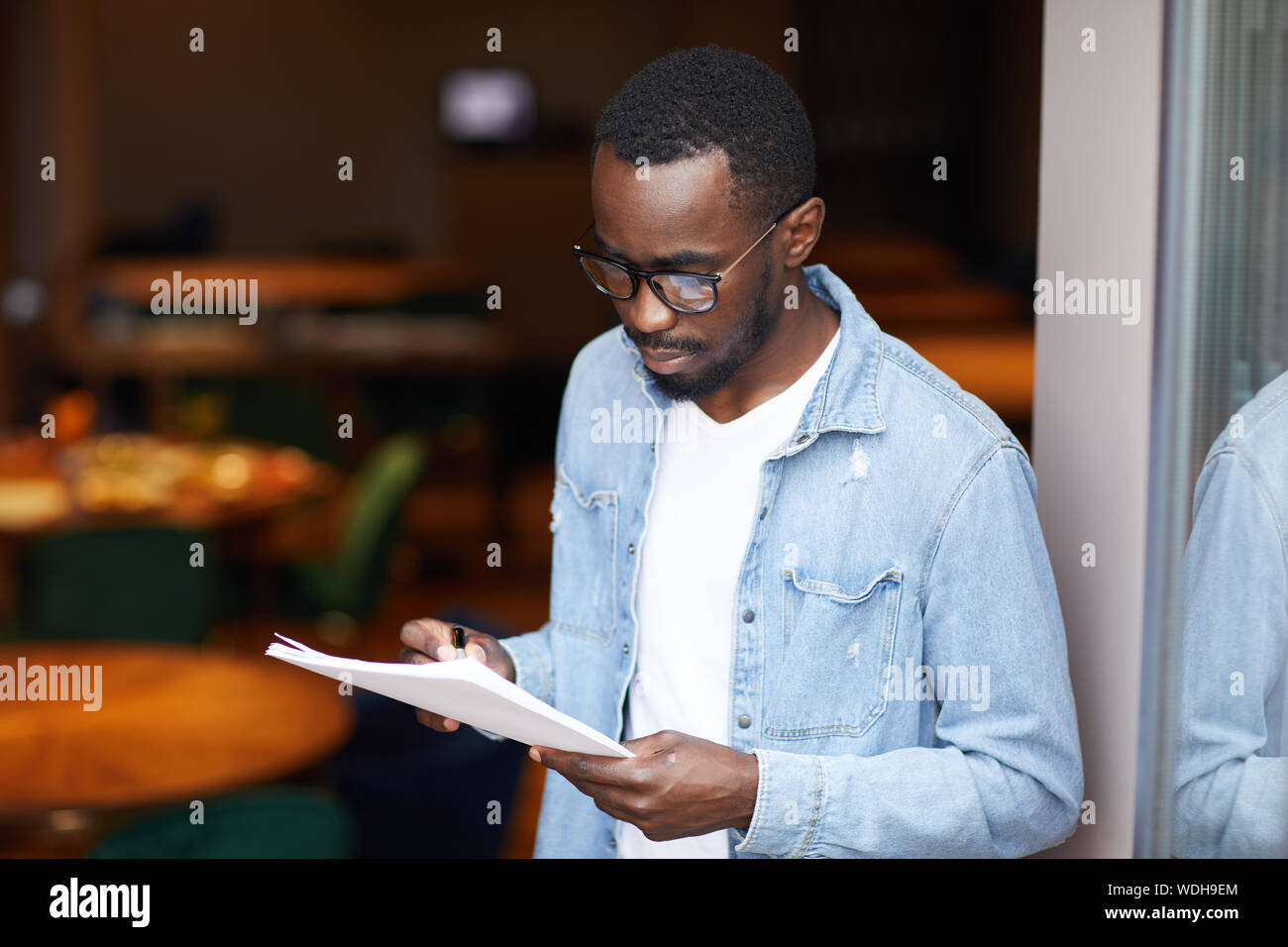 Junge afrikanische Menschen tragen Brillen ausfüllen, um die Dokumente in die Hände, während in der Nähe der Eingang im Restaurant stehen Stockfoto