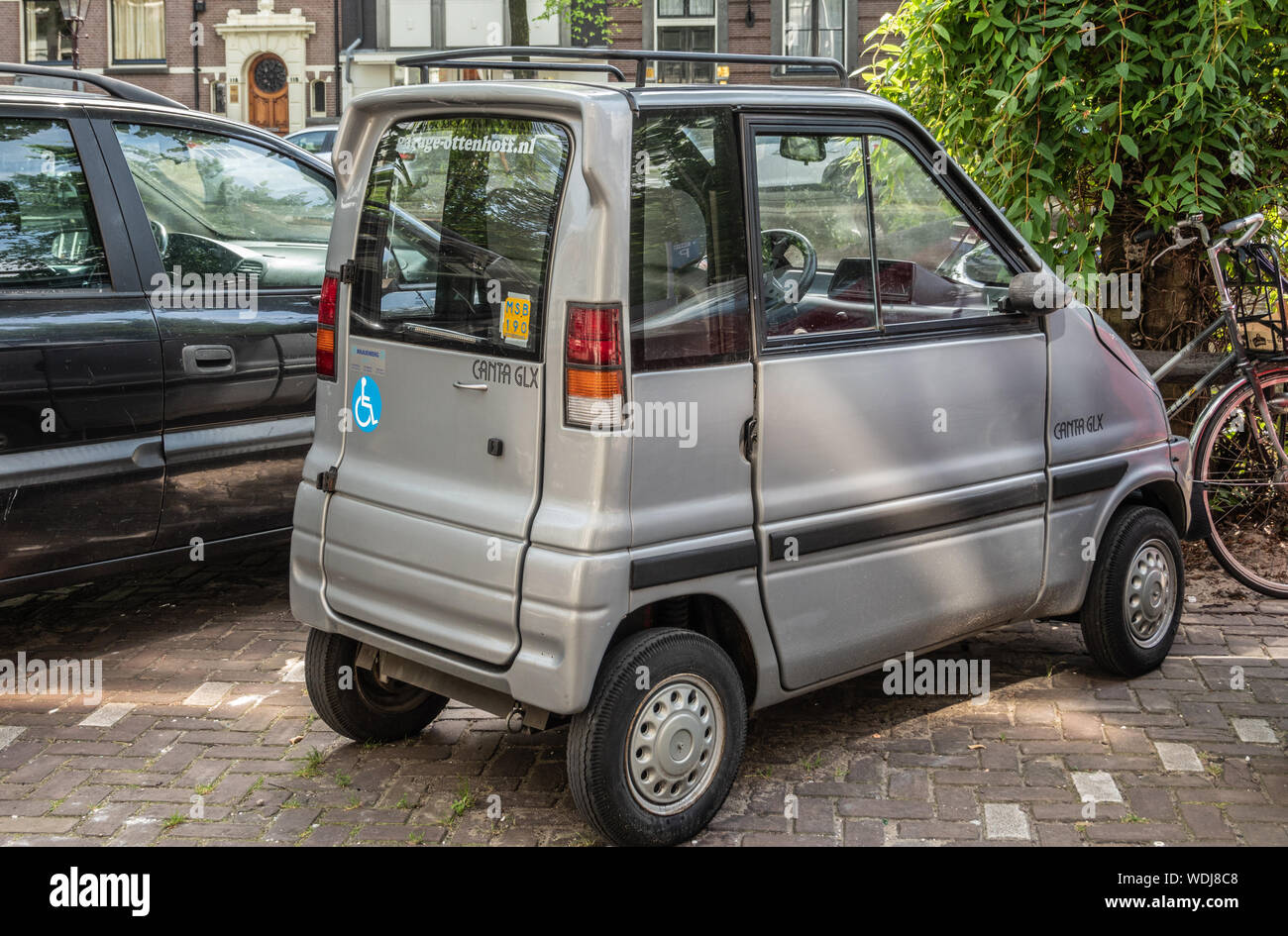 Amsterdam, Niederlande - 30. Juni 2019: Klein, Grau lackiert Mini Auto genannt Ganta GLX Canal geparkt. Grünes Laub. Stockfoto
