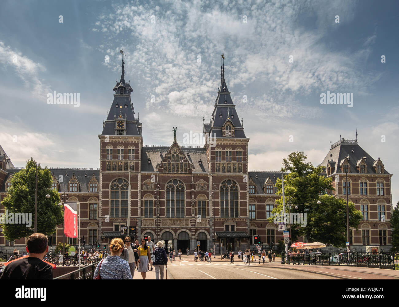 Amsterdam, Niederlande - 30. Juni 2019: Weite Einstellung der monumentalen Fassade mit Türmen in beige und roten Ziegeln. Statuen und Fresken. Unter blau-whtie Stockfoto