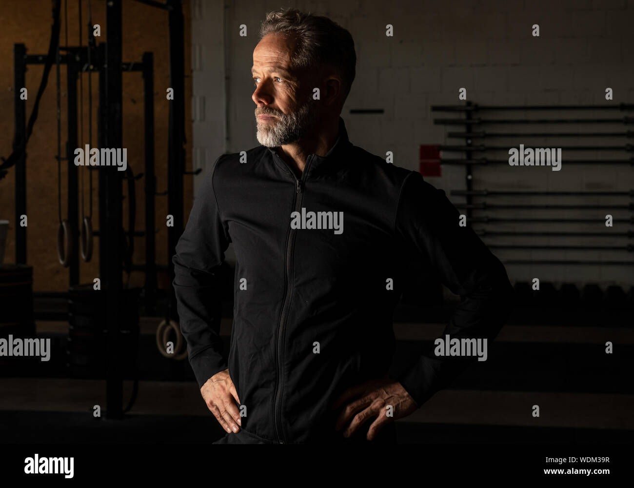Porträt eines attraktiven passen im mittleren Alter Mann in einem Fitness Studio. Bärtige grauhaariger Mann mit schwarzen Sweatshirt Jacke ist der Blick in die Ferne. Stockfoto