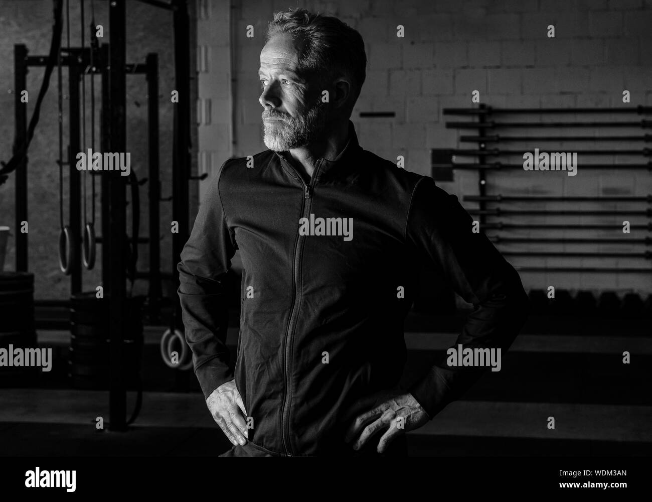 Porträt eines attraktiven passen im mittleren Alter Mann in einem Fitness Studio. Bärtige grauhaariger Mann mit schwarzen Sweatshirt Jacke ist der Blick in die Ferne. Stockfoto