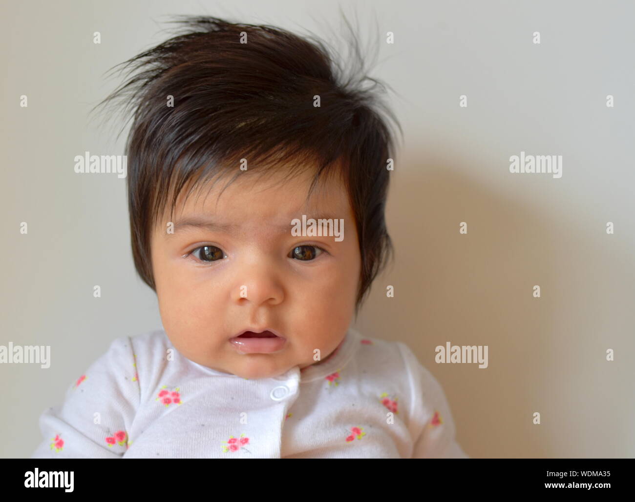 Sechs Monate alten Baby Mädchen mit langem Haar mit offenem Mund nach unten schauen. Stockfoto