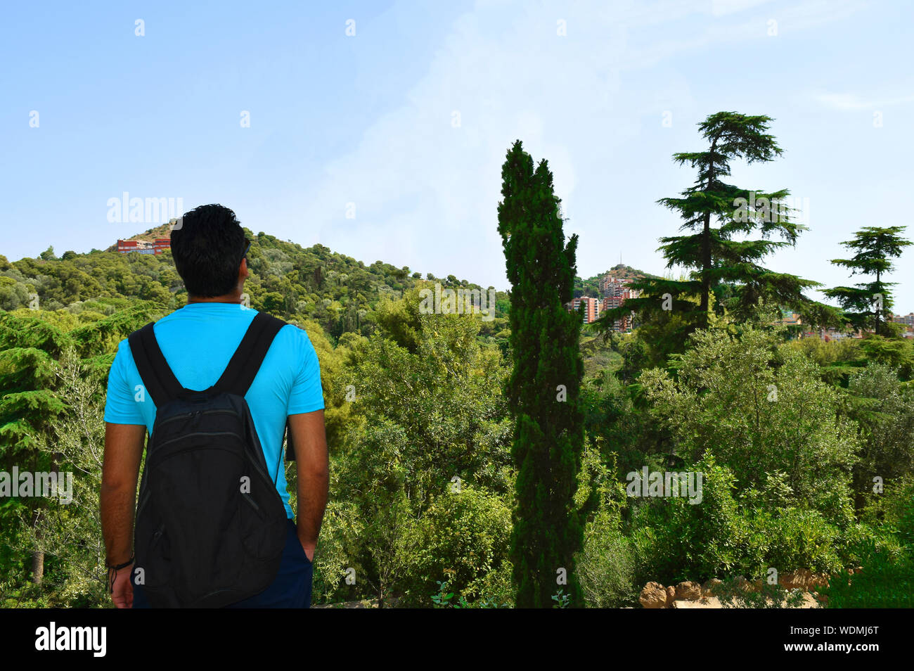 Junger Mann mit Rucksack Reisen befasst sich mit Panoramablick auf die Stadt in der Mitte des Waldes. Araber in Blau oder Türkis t-shirt mit Schwarz b Stockfoto