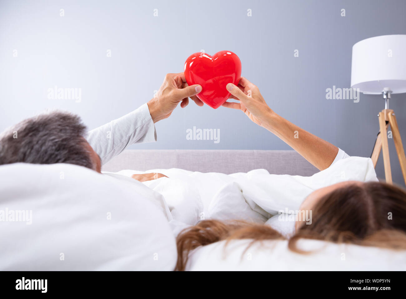 Paar liegend auf Bett mit weißer Decke halten roten Herzen in Ihren Händen Stockfoto