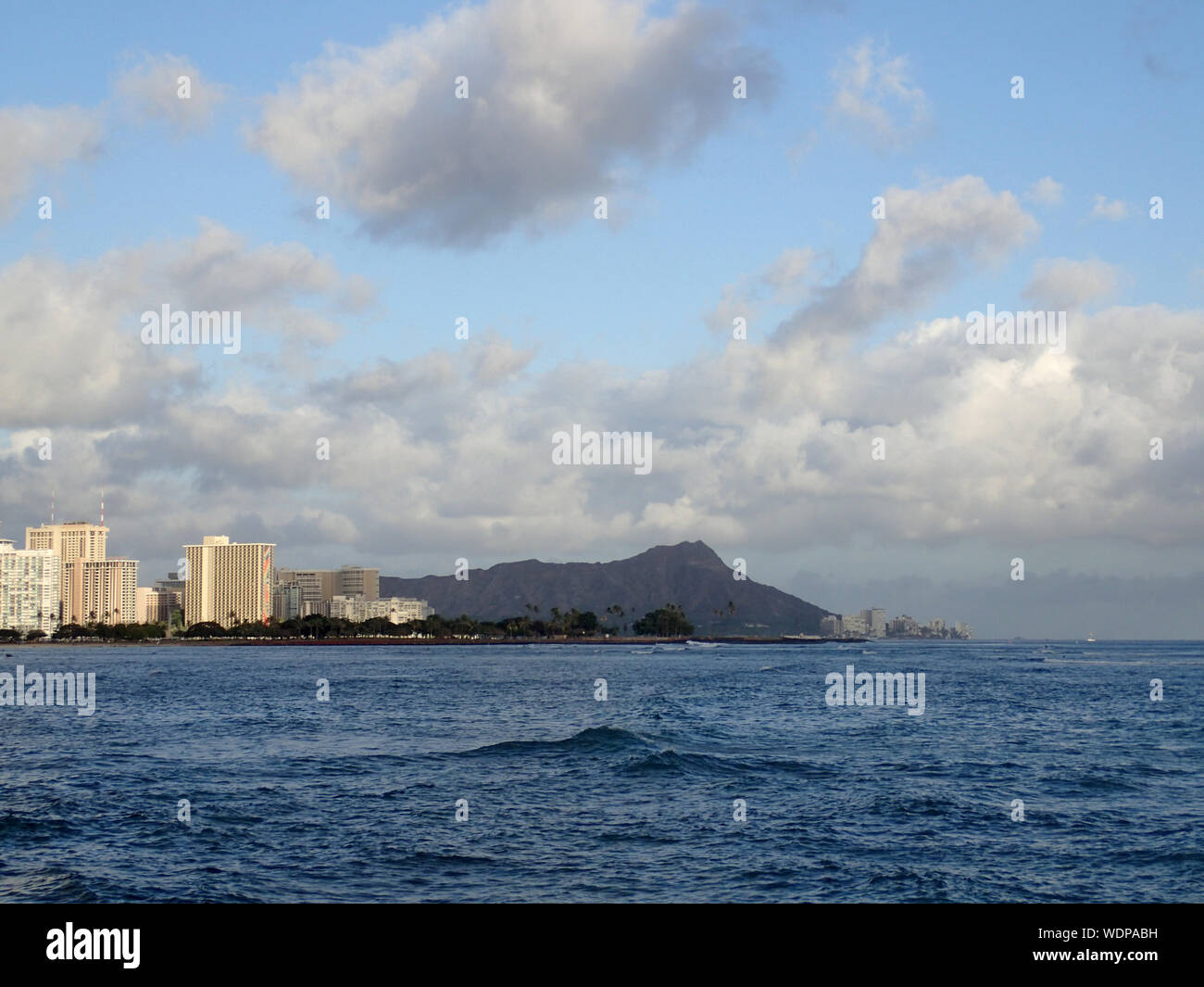 Wellen im Ala Moana Beach Park mit Waikiki und Diamond Head Krater, Bürogebäude und Eigentumswohnungen im Hintergrund, während Sie einen wunderschönen Tag auf der Insel Stockfoto