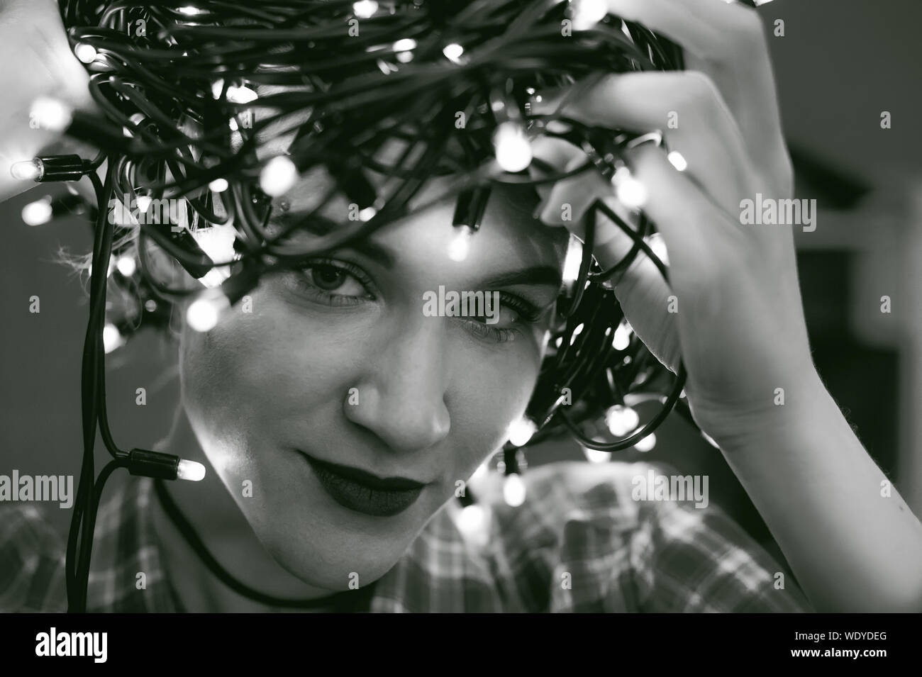 Nahaufnahme Porträt der jungen Frau mit glühenden String Scheinwerfer am Kopf zu Hause Stockfoto