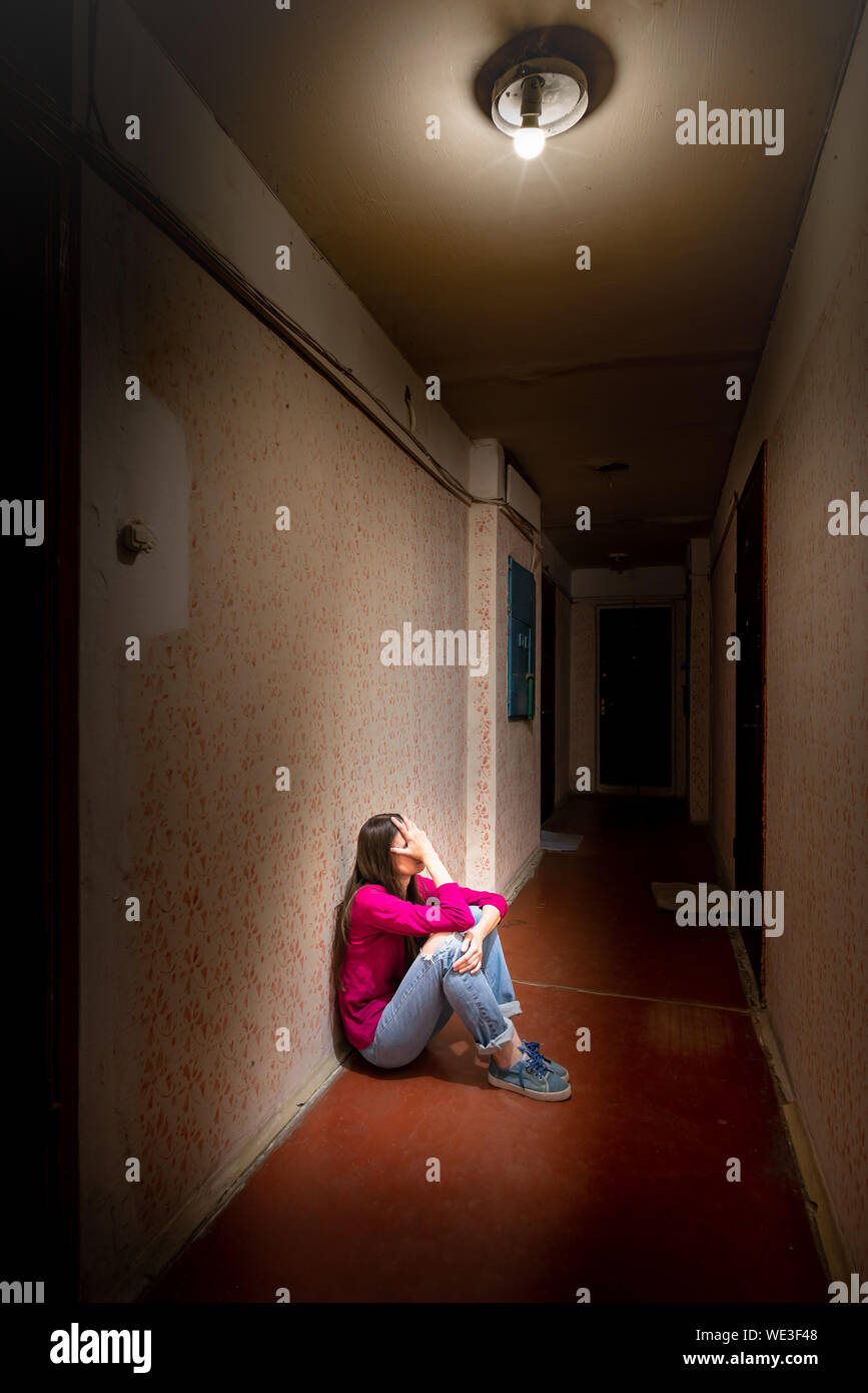 Eine traurige und verzweifelte Frau sitzt in einem dunklen Korridor durch ein düsteres Licht beleuchtet. Ihr Schmerz und ihre vielen Probleme drückte sie in die völlige Isolation. Hi Stockfoto