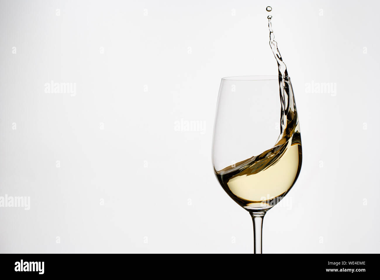 Weißwein Spritzer auf der Seite einer Elegante lange wineglass in einem freeze motion Bild einen weißen Hintergrund stammt Stockfoto