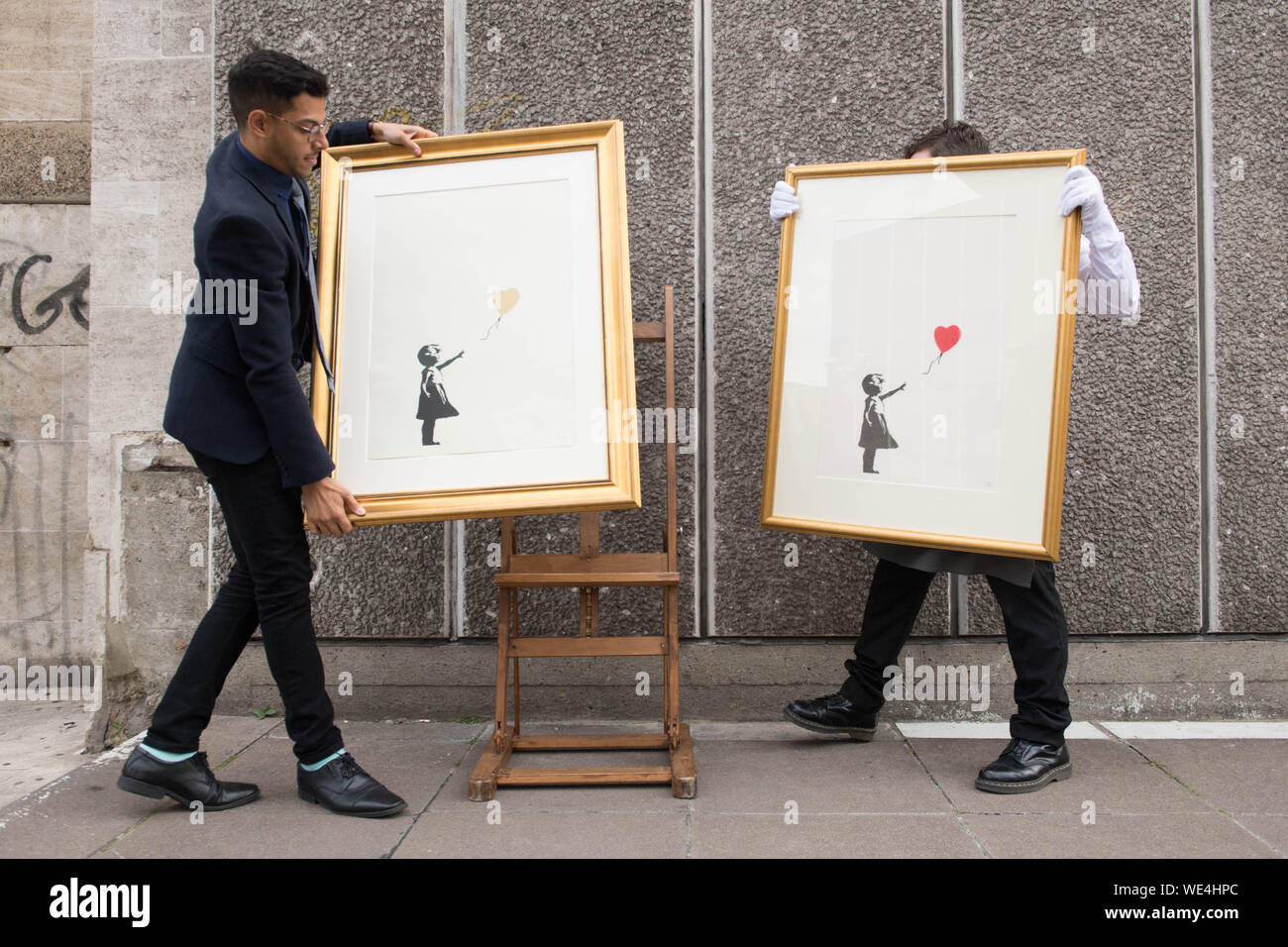 Mitarbeiter des Auktionshauses Christie's mit zwei Versionen von ÔGirl with Balloon' des anonymen Straßenkünstlers Banksy, in der Nähe eines der Orte, an denen das Kunstwerk ursprünglich auf der Southbank in London erschien. Die Bilder sollen in einer Online-Auktion verkauft werden, ÔBanksy: Ich kann nicht glauben, dass ihr Morone tatsächlich dieses sh*t' kauft, das vom 11. Bis 24. September stattfinden wird. Stockfoto