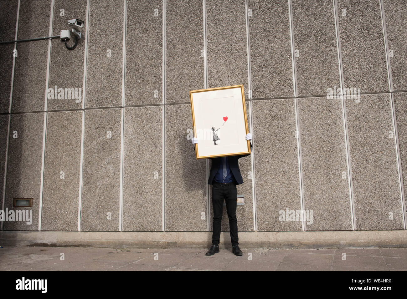 Mitarbeiter des Auktionshauses Christie's mit einer Version von ÔGirl with Balloon' des anonymen Straßenkünstlers Banksy, in der Nähe eines der Orte, an denen das Kunstwerk ursprünglich auf der Southbank in London erschien. Das Bild soll in einer Online-Auktion verkauft werden, ÔBanksy: Ich kann nicht glauben, dass ihr Morone tatsächlich dieses sh*t' kauft, das vom 11. Bis 24. September stattfinden wird. Stockfoto