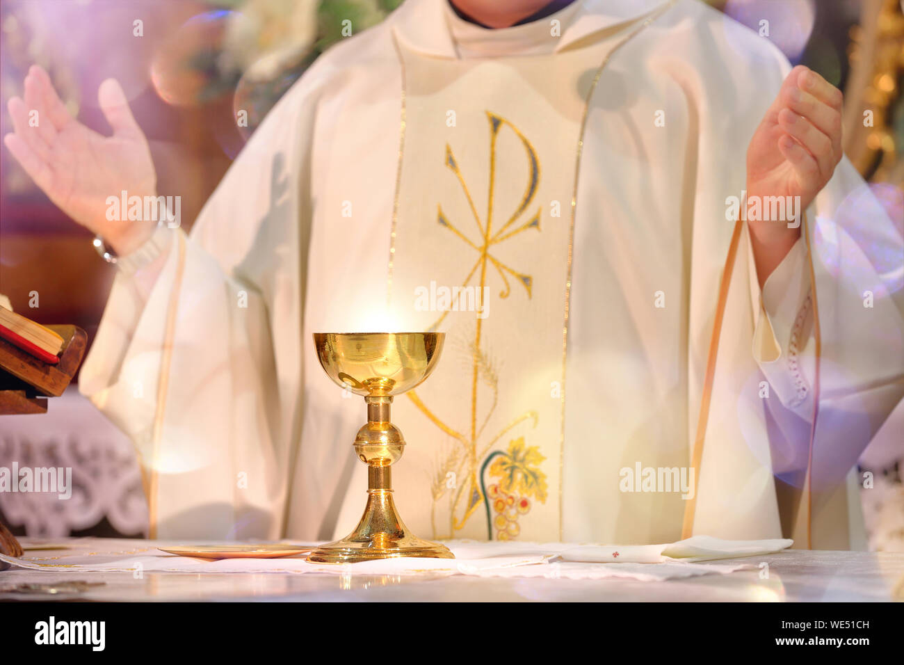 Kelch auf dem Altar mit Lichtstrahlen und Priester feiern Stockfoto