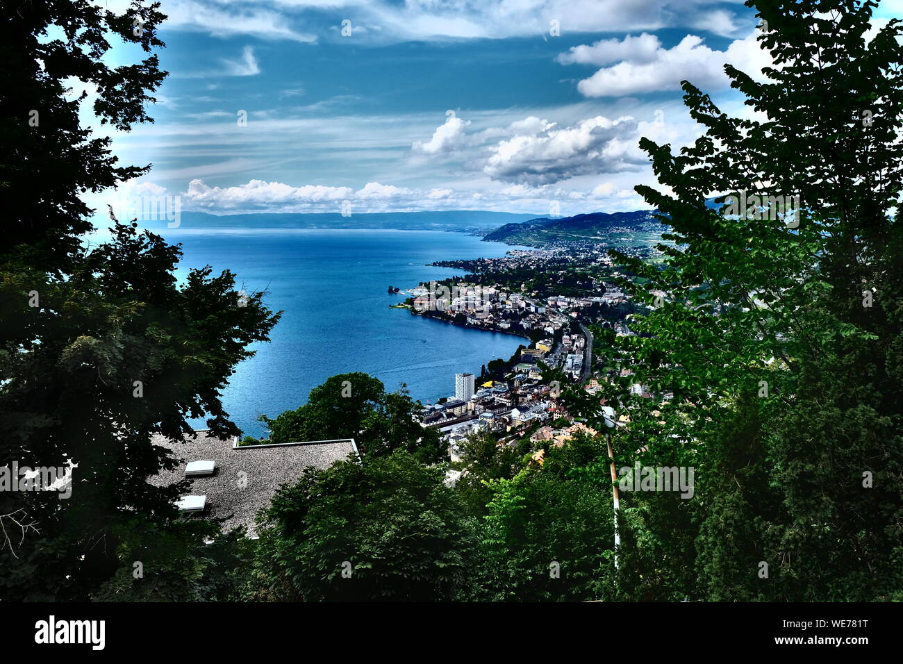 Hochwinkel-Panorama über Montreux und das Ufer des Genfer Sees, eingerahmt von üppigen grünen Bäumen unter einem dramatischen bewölkten Himmel, Waadt, Schweiz Stockfoto