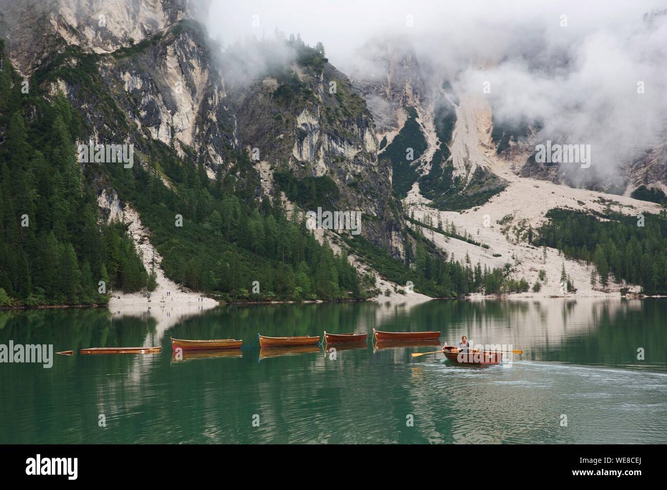 Italien, Autonome Provinz Bozen, Prags, Frau Rudern in einem Boot auf dem See mit smaragdgrünen Gewässern durch Berge im Nebel gefangen umgeben Stockfoto