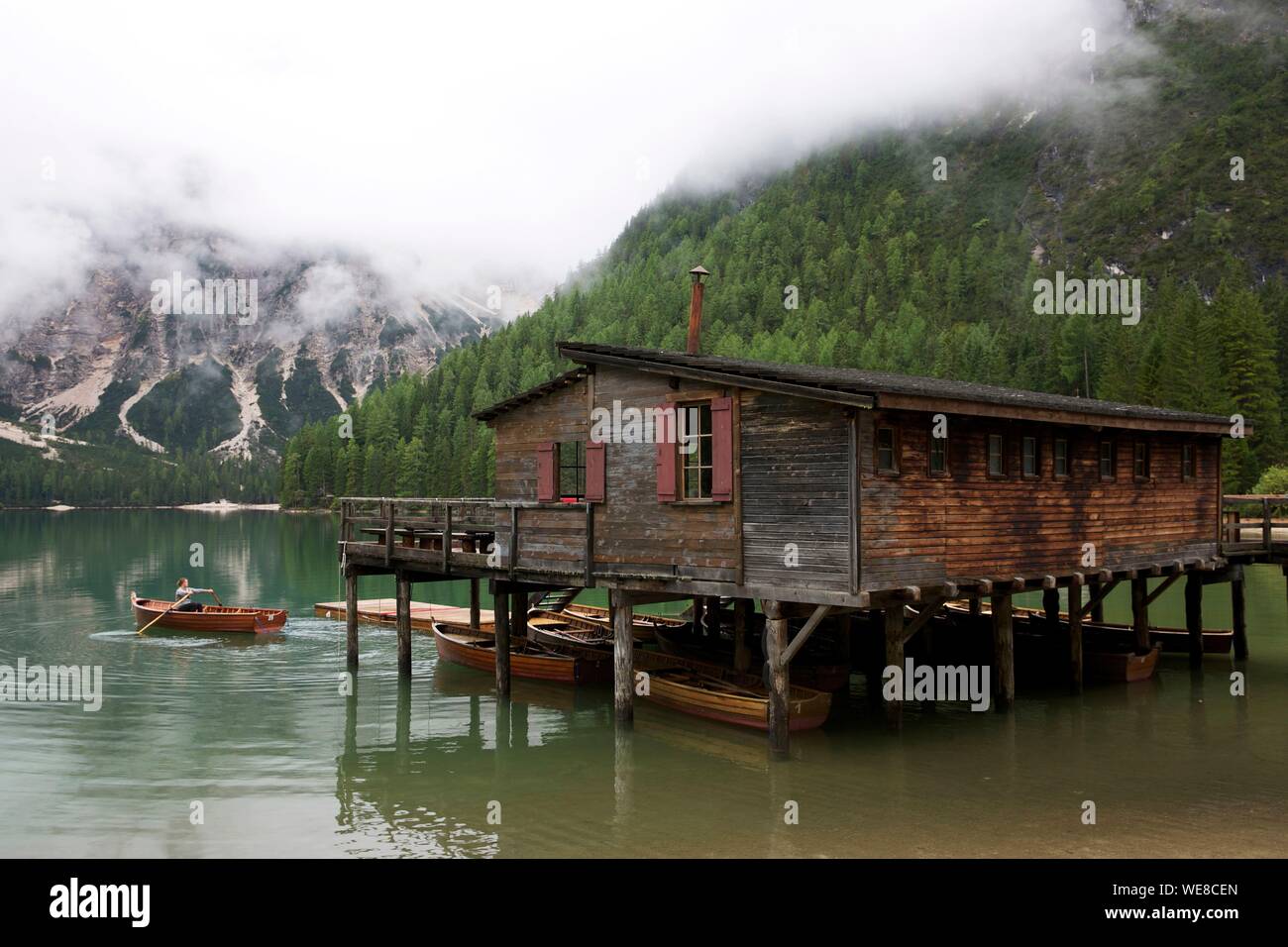 Italien, Autonome Provinz Bozen, Hochpustertal Tal, See von Prags, Frau Rudern in einem Boot vor ein Holzhaus auf Stelzen über den smaragdgrünen Gewässern der See durch die grünen Berge im Nebel gefangen umgeben Stockfoto