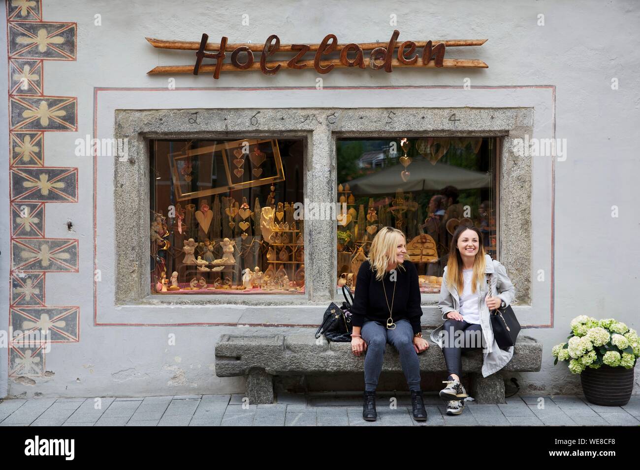 Italien, Autonome Provinz Bozen, Bruneck, zwei Frauen sitzen auf einer Steinbank vor einem Handwerksbetrieb in der Innenstadt und der Gasse Stockfoto