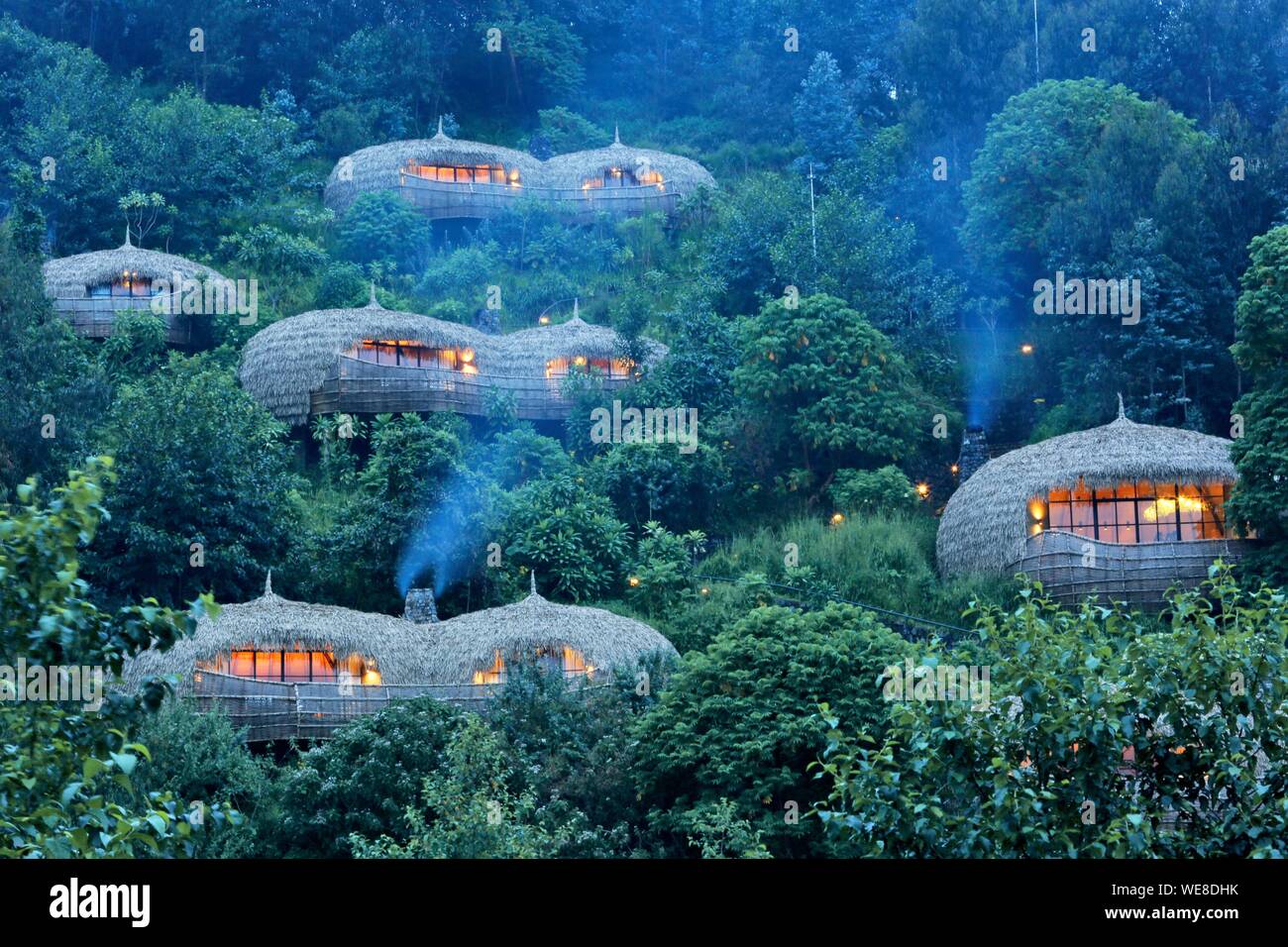 Ruanda Volcanoes National Park, strohgedeckten Villen der Wildreness Bisote Lodge Safaris Hotel Gruppe, die sich aus einem Hügel bedeckt mit Vegetation Stockfoto