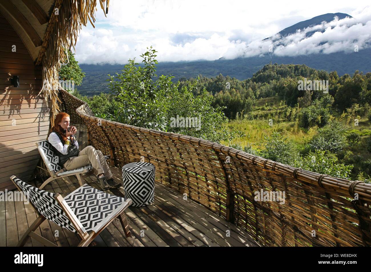Ruanda Volcanoes National Park, Frau trinkt Tee auf der Terrasse der Suite in Bisate Lodge, eine Lodge der Wilnderness safaris Hotel Group, öffnen Sie auf dem Berg Bisoke Stockfoto