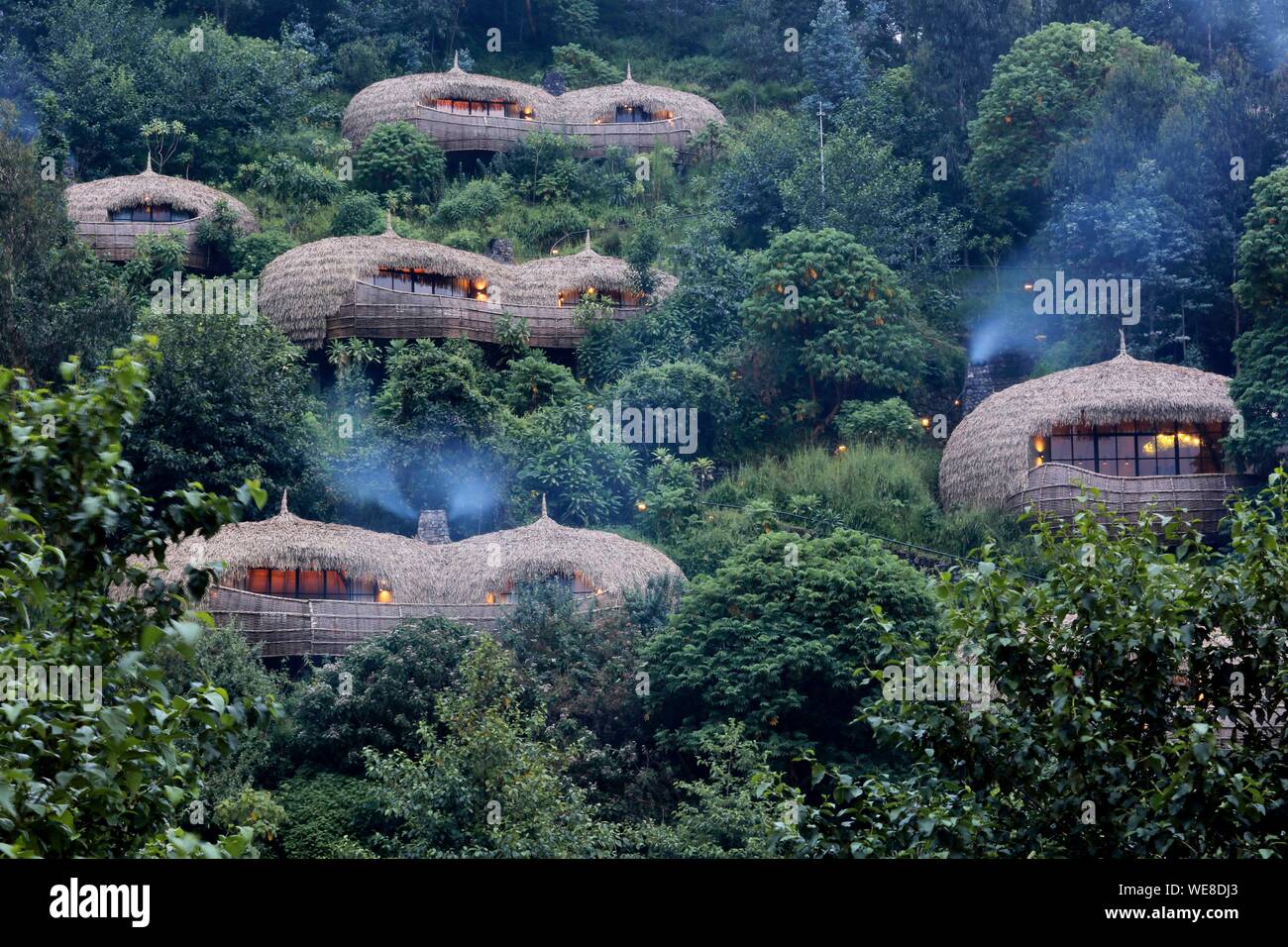 Ruanda Volcanoes National Park, strohgedeckten Villen der Wildreness Bisote Lodge Safaris Hotel Gruppe, die sich aus einem Hügel bedeckt mit Vegetation Stockfoto