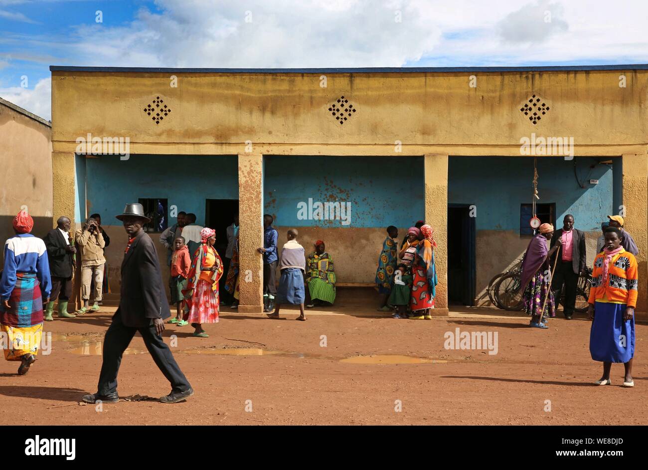 Ruanda, Zentrum des Landes, Dorfbewohner in farbenfrohe Outfits vor einem säulengang Gebäude in einem Dorf mit unbefestigten Straßen Stockfoto