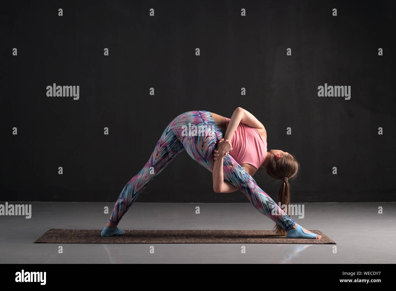 Junge Frau, Variation von Trikonasana yoga Pose, Studio voller Länge Rückansicht Stockfoto