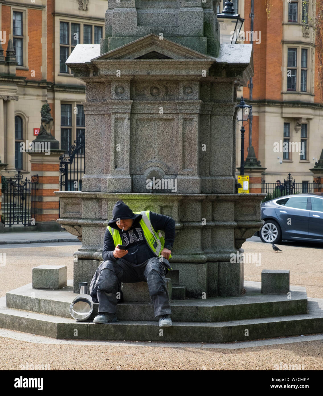 Bauarbeiter raucht und sieht bei seinem Telefon zu kunstvollen Twells Memorial Brunnen in der Nähe von Lincoln's Inn Fields, London sitzen. Im Jahr 1880 errichtet. Stockfoto